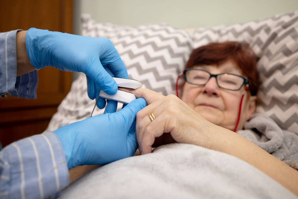 Test oxymétrique patient âgé dans la prévention de la pneumonie à Covid 19 dans une maison de soins infirmiers, médecin examinant la femme âgée à l'aide d'oxymètre à la maison - Photo, image