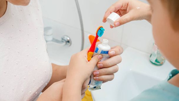 Closeup of mother helping her toddler son applying tooth paste. Child using toothbrush and toothpaste for brushing and cleaning teeth - Fotografie, Obrázek