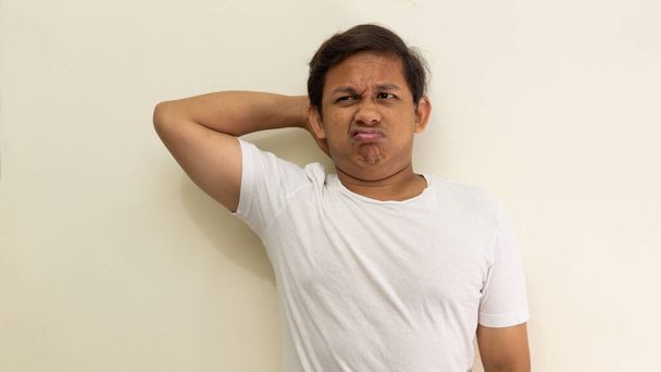 Confused and bewildered face expression with hand behind head of young Asian Malay man with white t-shirt on isolated white background. Confuse hand gesture. - Photo, Image