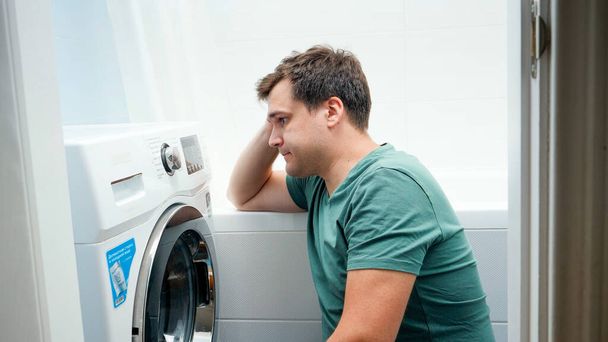 Retrato de un joven que lucha y se confunde al configurar la lavadora para la ropa - Foto, Imagen