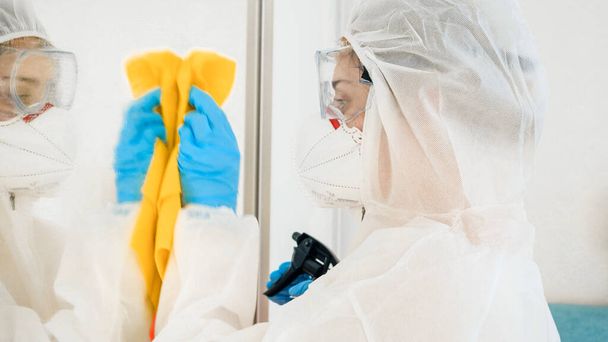 Bacteriologist or cleaning worker in bioazard protective suit washing house with chemical detergent and desinfecting furniture - Photo, Image