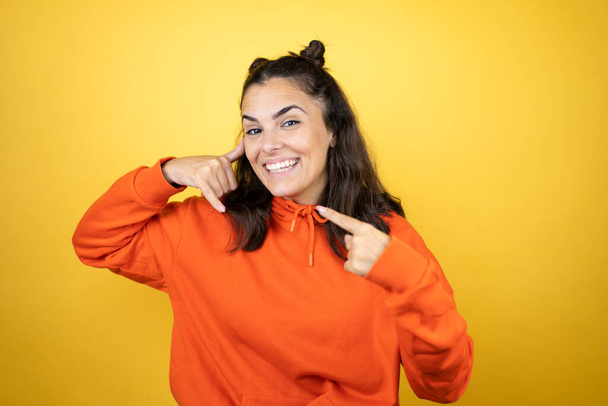 Young beautiful woman wearing sweatshirt over isolated yellow background doing the call me gesture with her hands - Photo, image