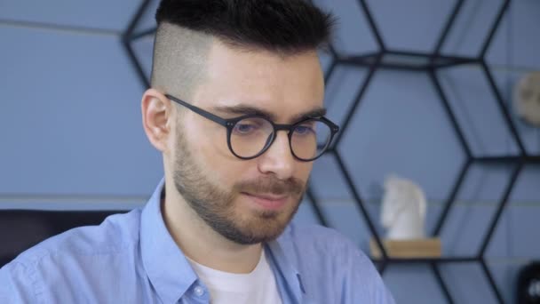 Zbliżenie portret przystojnego mężczyzny noszącego okulary patrzącego na laptopa pracującego w biurze - Materiał filmowy, wideo
