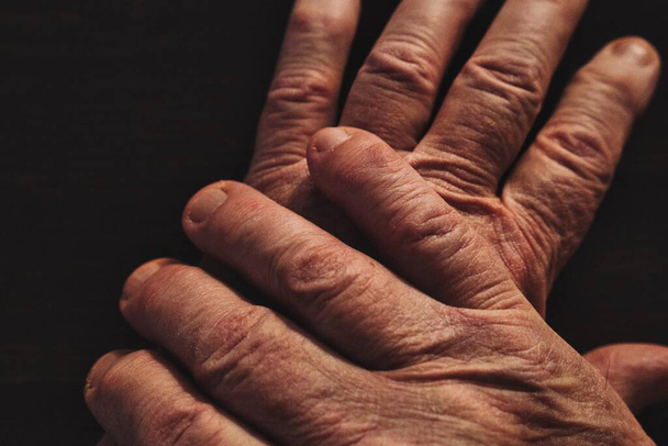 Wrinkled hands of old man on top of each other. Close up. High angle view.  - Фото, изображение