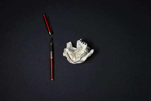 Crumpled paper and a red pen lie on a black background. Creative crisis. Lack of ideas.  - Foto, Bild