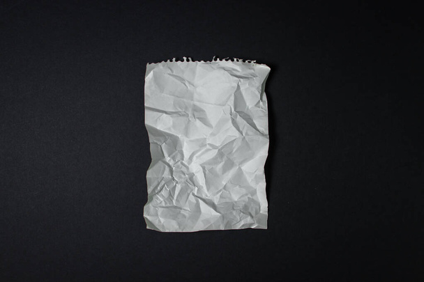 Ένα τσαλακωμένο φύλλο χαρτιού σε μαύρο φόντο. Δημιουργική κρίση. Έλλειψη ιδεών. Ιστορικό γραμμάτων ή λογότυπου - Φωτογραφία, εικόνα