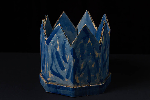 黒の背景に厚紙の王冠。紙製品。偽の王冠。ずさんな青い王冠。嘘の力 - 写真・画像