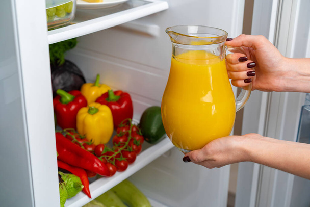 Female hand taking orange juice jar from a fridge - Foto, afbeelding