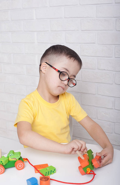 Chłopiec w okularach z zespołem Downa siedzi przy stole i bawi się zabawkami - Zdjęcie, obraz