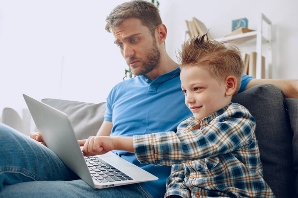 Father and son sitting on couch and watching something on laptop - Foto, afbeelding