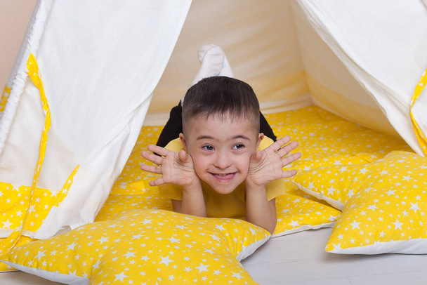 Portré egy aranyos fiú Down-szindrómával ül egy sárga kunyhóban - Fotó, kép