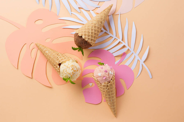 Három különböző ízű fagylalt tölcsérek feltéttel és pálmalevelek pasztell rózsaszín háttér. Trópusi nyári koncepció. Felülnézet, másolás. - Fotó, kép