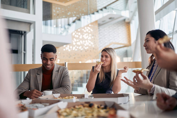 A group of employees eating pizza in a break at company's canteen in a pleasant atmosphere. People, job, company, business concept. - Foto, Imagen
