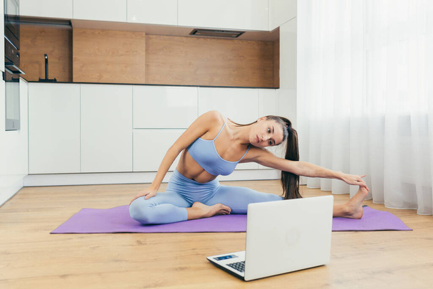 Beautiful fitness woman doing fitness exercises, looking for online tutorials on laptop, training in the kitchen. Healthy Lifestyle. The girl goes in for sports at home. - Photo, Image