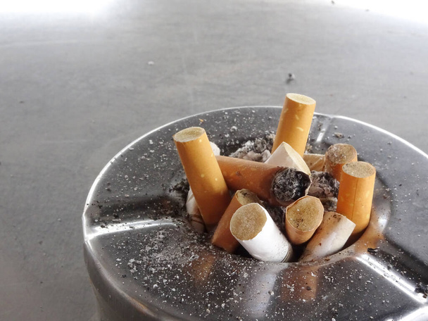 gebrauchter Zigarettenstummel im schmutzigen Edelstahl-Aschenbecher.   - Foto, Bild