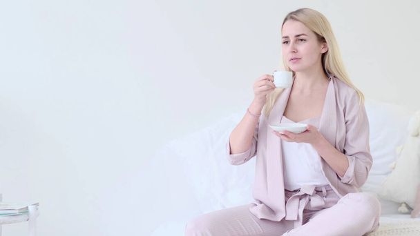 gyönyörű fiatal nő egy csésze kávéval, romantikus környezetben. Elölnézeti nő kávéscsészével a kanapén ülve a kamerát nézi. szelektív fókusz. - Fotó, kép
