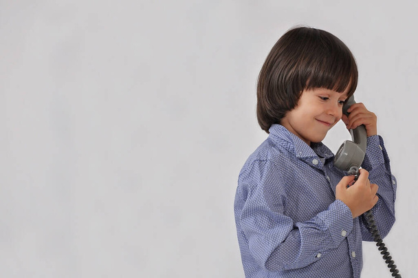 a isolated little european boy talking on an vintage phone smiling looking down - Photo, Image