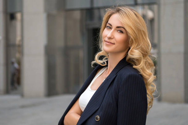 Блондинка в темно-синем классическом костюме smart-casual на улице возле высокотехнологичного бизнес-здания. Пространство для текста - Фото, изображение