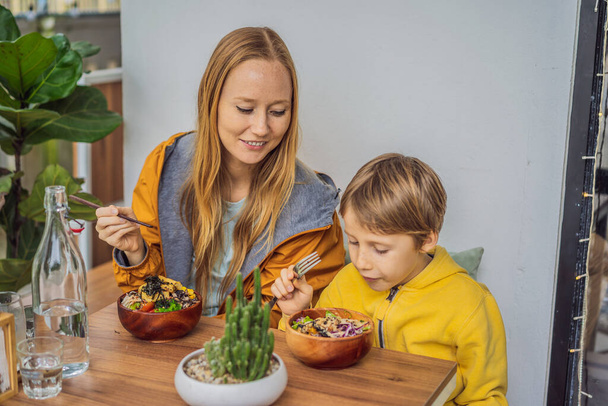 Madre e figlio mangiano Raw Organic Poke Bowl con riso e verdure primo piano sul tavolo. Vista dall'alto orizzontale - Foto, immagini