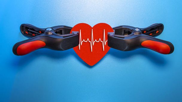 Healthcare and medicine concept - close up of a red heart with an ecg line clamped in a vise for resuscitation. Salvation of life and feelings. Valentine's Day. - Photo, Image