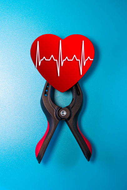 Healthcare and medicine concept - close up of a red heart with an ecg line clamped in a vise for resuscitation. Salvation of life and feelings. Valentine's Day. - Photo, Image