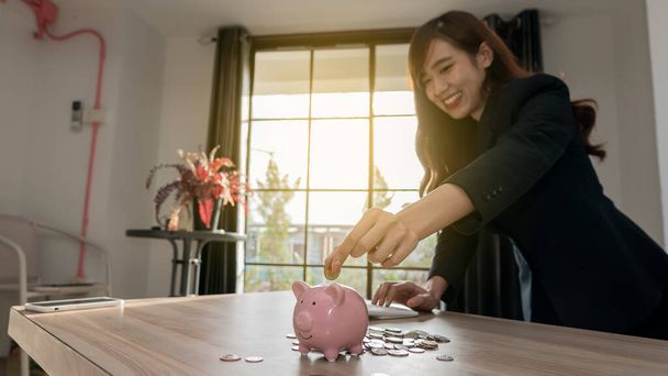 Nő kezében egy érme egy malac bank rózsaszín disznó és egy halom érme az asztalon egy pénztakarékos koncepció számológép - Fotó, kép
