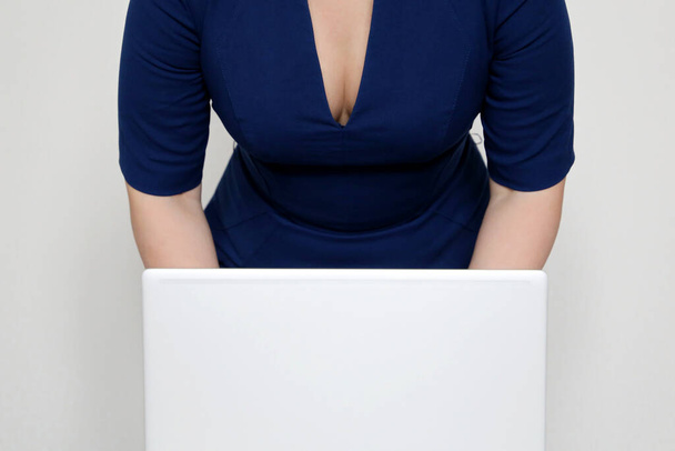 Woman in a blue dress with a plunging neckline bent over laptop. Concept of sexy secretary, dress code in the office - Fotografie, Obrázek
