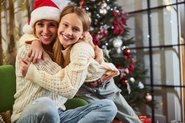 Joyful meisje knuffelen met mam met Kerstmis binnen - Foto, afbeelding
