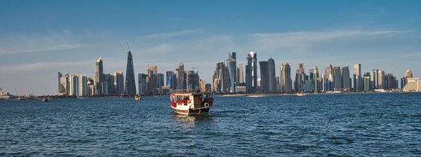 horizonte de Doha desde el paseo corniche tiro de la tarde mostrando dhow con la bandera de Qatar en el golfo árabe en primer plano y las nubes en el cielo en el fondo - Foto, imagen