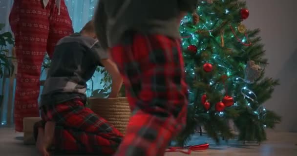 Eine Familienmutter und zwei Kinder schmücken im Wohnzimmer ihres Hauses einen Weihnachtsbaum mit Spielzeug. Weihnachtsdekoration und Vorbereitung auf das Fest - Filmmaterial, Video