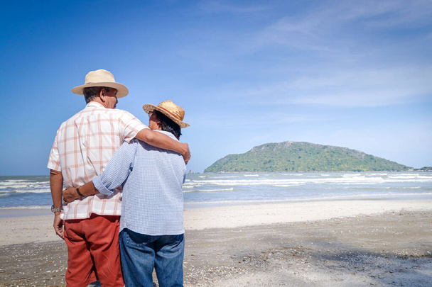 Starší asijský pár objímající se na pláži. Podívej se na to krásné moře. Cestovní koncept Žij šťastný život v důchodu. kopírovat prostor - Fotografie, Obrázek