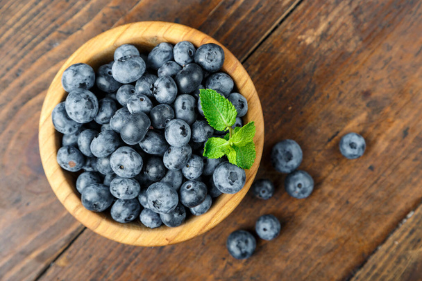 Freshly picked blueberries in wooden bowl on wooden background.  Concept of healthy and dieting eating. Tasty food. - Photo, image