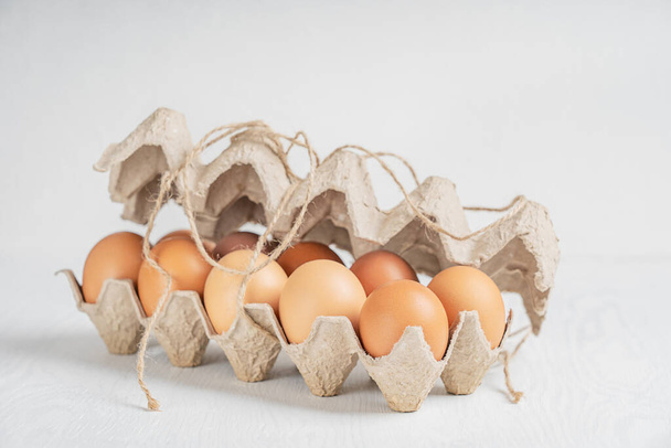 Close-up view of raw brown fresh chicken eggs in container made of recycled paper on white wooden background. Healthy eating and sustainable consumption concept. Horizontal image - Zdjęcie, obraz