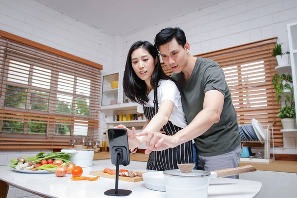 Le coppie asiatiche hanno la gioia di cucinare in cucina a casa. Guarda i video tutorial realizzati online tramite smartphone. Concetto di cibo. copia spazio - Foto, immagini