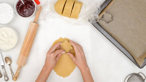 花形のショートブレッドクッキーにラズベリージャムのレシピが詰まっています。クッキーカッターを使ってクッキーをスタンプする女性の手 - 写真・画像