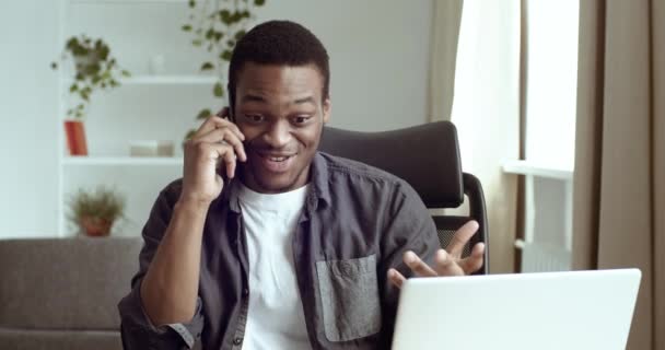 Portret szczęśliwego afrykańskiego biznesmena amerykańskiego sprzedawcy, studenta rozmawiającego przez smartfon wygrywa, poznaje dobre wieści, dostaje szansę, nowa praca mówi, że tak, to przyjemność siedzieć przy stole w biurze lub w domu. - Materiał filmowy, wideo
