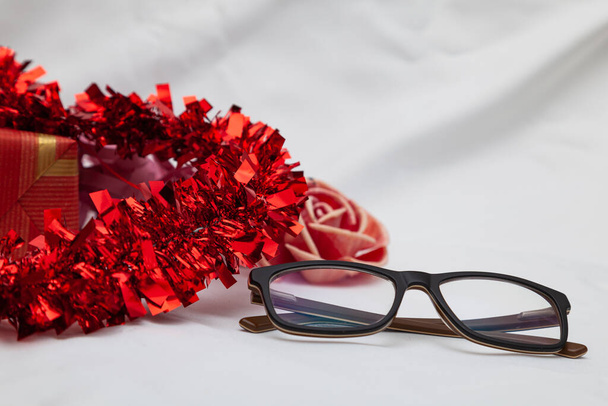 Některé sklenice vedle dekorativního červeného srdce, které nelze vidět celé, dárek a květinu. V pozadí je bílá látka. - Fotografie, Obrázek