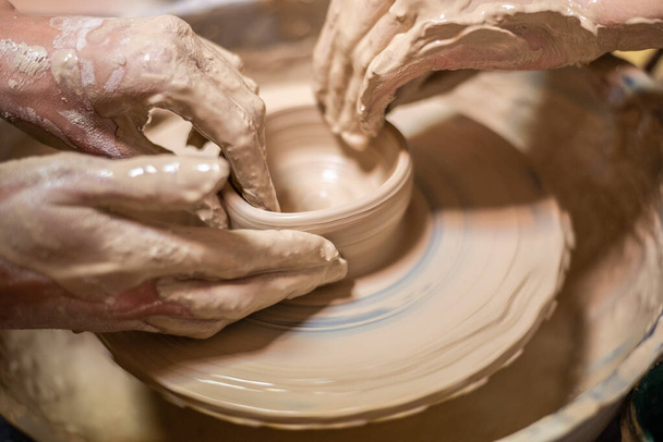 Vrouwelijke pottenbakker werkt aan klei op een pottenbakkerswiel, handen dicht. Een handgemaakte kleipot maken in de werkplaats. Aardewerk les, hobby. - Foto, afbeelding