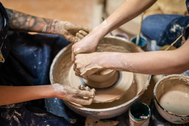 Female potter working on clay on a potter's wheel, hands close up. Making a handmade clay pot in the workshop. Pottery lesson, hobby. - Photo, Image