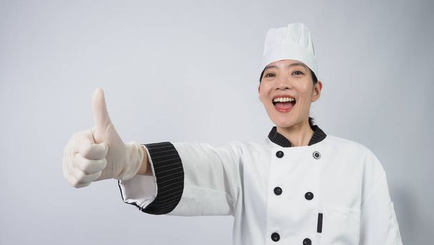 シェフのジェスチャー。ポートレート美しいアジアの女性は、帽子をかぶって調理し、シェフの制服はジェスチャーサインを作り、カメラを見ています。インフルエンサー。料理教室。コピースペース。オンライン食品商人のシェフ. - 写真・画像