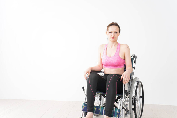 Genç bir kadın spor kıyafetleriyle tekerlekli sandalyeye biniyor. - Fotoğraf, Görsel