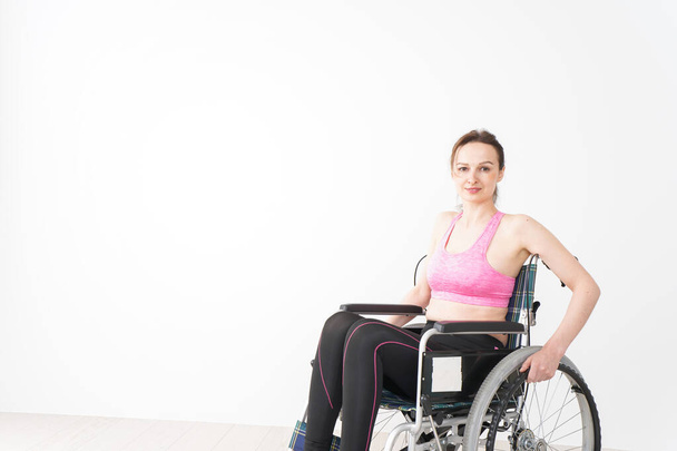 Genç bir kadın spor kıyafetleriyle tekerlekli sandalyeye biniyor. - Fotoğraf, Görsel