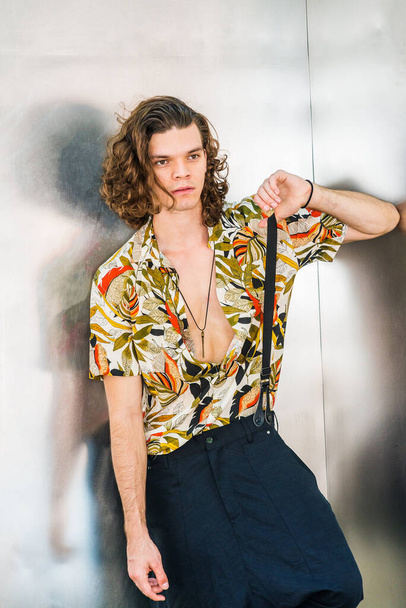 Portrait of Young Hispanic American Man in New York City, with long brown curly hair, wearing colorful patterned short sleeve shirt, hanging old key as necklace, one black pants suspender on shoulder - Foto, Imagem
