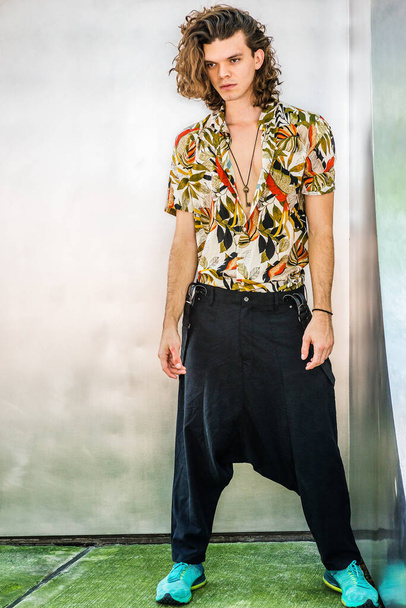 Artista hispânico americano com cabelo encaracolado marrom em Nova York, vestindo camisa de manga curta estampada colorida, calças soltas largas com suspensórios, tênis estampados, pendurado chave velha como colar - Foto, Imagem