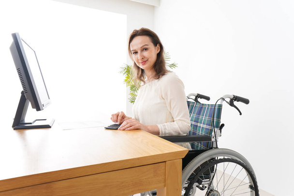 Junge Frau erledigt Schreibtischarbeit im Rollstuhl - Foto, Bild