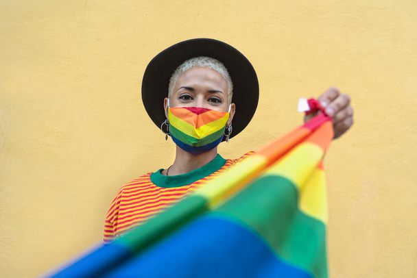 ゲイの誇りマスクを身に着けている若い女性保持虹旗シンボルのLgbtq社会運動 - 写真・画像