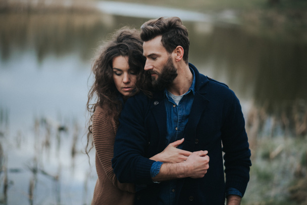 Két kaukázusi szerető a tó mellett. A fiatal pár ősszel a szabadban ölelkezik. Egy szakállas férfi és egy göndör nő szerelmes. Valentin nap. A szeretet és a család fogalma. - Fotó, kép
