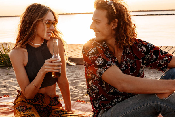 Image of a happy positive young loving couple drinking beer at the beach - Photo, image
