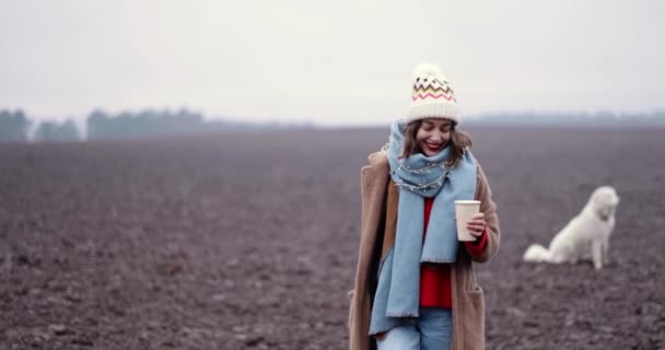 Femme marchant avec une tasse de café et jouant avec son chien sur le terrain en hiver - Séquence, vidéo
