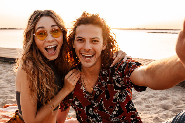 Photo of excited cheery young loving couple at the beach taking a selfie by camera - Фото, изображение